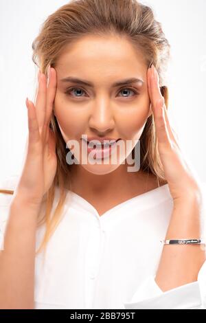 Meravigliosa bella donna con pelle morbida pulita senza trucco, labbra grandi, occhi blu. Volume capelli biondi. Toccare il viso. Dita tenera con maniaco Foto Stock