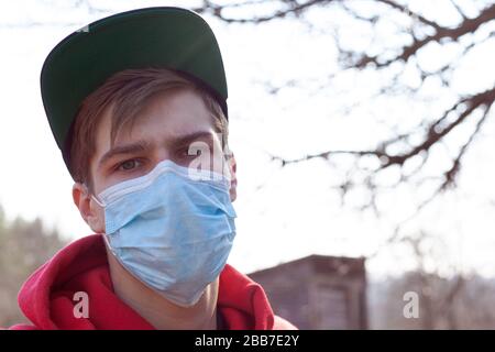 il ragazzo vestito di rosso sta in piedi nella strada in una maschera medica da vicino, impedendo la diffusione del virus covid-19, concetto di salute. Foto Stock