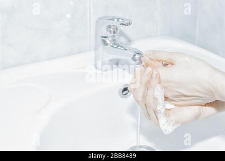 Donna sta pulendo le sue mani con sapone sotto acqua nel bagno. Foto Stock