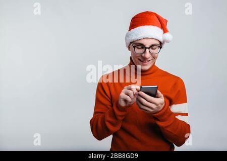Felice bel uomo di natale cappello guarda il suo smartphone. Foto Stock