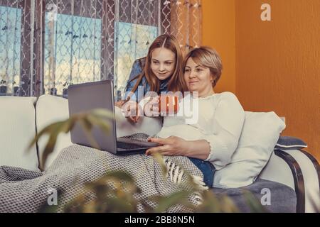 Madre e sua figlia adolescente che guardano contenuti on line in un computer portatile in un soggiorno a casa. Foto Stock