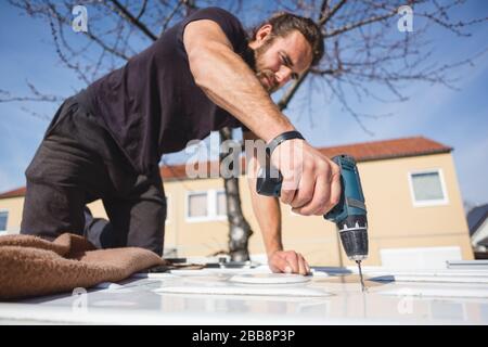 Uomo che perfora un buco nel tetto del suo camper van Foto Stock