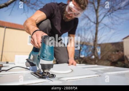 Uomo che taglia un buco nel tetto del suo camper van Foto Stock