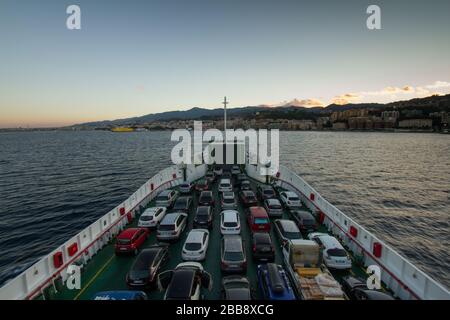 Vista dello Stretto di Messina e del porto di Messina, dal traghetto che la attraversa, con auto e camion all'interno del traghetto stesso Foto Stock