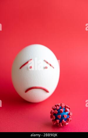 Modello di coronavirus plastificato e isolato di uovo su sfondo rosso. Modello plastilina di coronavirus e uovo di pasqua raffigurante paura e tristezza. Grande Foto Stock