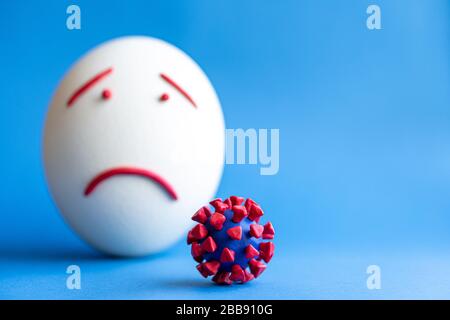 Modello di coronavirus plastificato e isolato di uovo su sfondo blu. Modello plastilina di coronavirus e uovo di pasqua raffigurante paura e tristezza. Grande Foto Stock