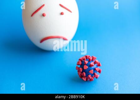 Modello di coronavirus plastificato e isolato di uovo su sfondo blu. Modello plastilina di coronavirus e uovo di pasqua raffigurante paura e tristezza. Grande Foto Stock