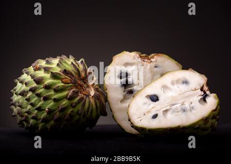 Soursop o Graviola con buccia verde vibrante di prickly e ha aperto il campione con polpa bianca e semi duri neri che mostrano. Monolocale a bassa chiave Foto Stock