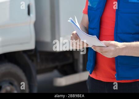 Corriere in uniforme prendendo appunti nel documento e consegna camion bianco lo behinde Foto Stock
