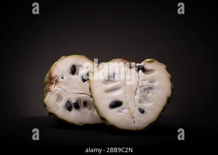 Aperto Soursop o Graviola frutta che mostra la sua polpa bianca e semi neri duri. Monolocale a bassa chiave con cibi freschi. Foto Stock