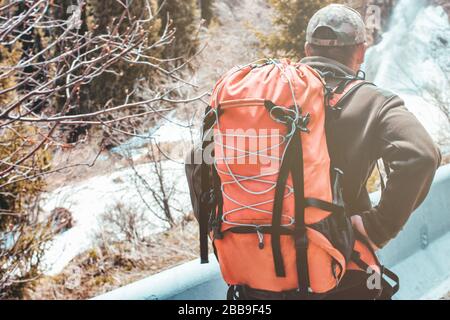 Uomo escursioni in montagna con grande zaino arancione da viaggio. Uomo viaggiatore in cappello trekking durante il suo viaggio. Viaggi, persone, sport e stile di vita sano Foto Stock