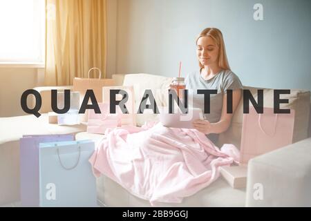 Shopping online a casa. Giovane donna bionda con il tè sta guardando il tablet e la scelta di prodotti in negozio online, mentre seduta con coperta su un divano marrone Foto Stock