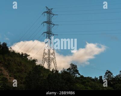 Una torre di trasmissione su una collina rocciosa verde con uno sfondo blu cielo. Foto Stock