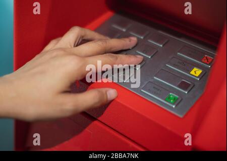 Donna mani per premere il tasto ATM nel cabinet rosso. Dito che preme un codice pin su un tastierino numerico. Codice di sicurezza su una macchina di teller automatica rossa ( Foto Stock