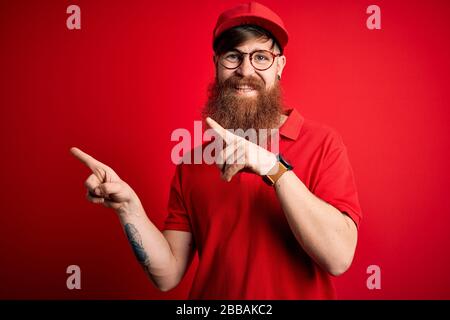 Giovane e bel uomo che indossa occhiali e tappo rosso su sfondo isolato sorridente e guardando la fotocamera che punta con due mani e dita Foto Stock