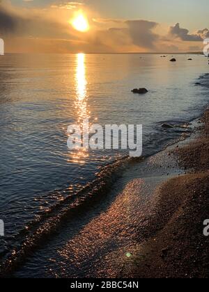 La costa al tramonto, il tramonto pittoresco, l'acqua tranquilla, una spiaggia sabbiosa, le nuvole sono illuminate dal sole del tramonto, riflessione speculare in acqua Foto Stock