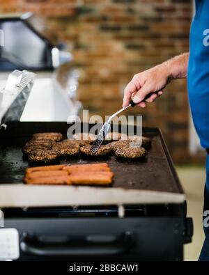 Cottura, grigliatura di hamburger e hot dog durante l'isolamento, quarantena a causa di COVID-19 e coronavirus Foto Stock