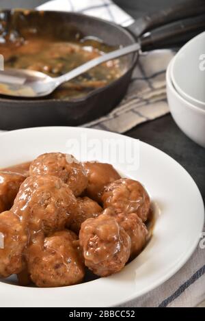 Una ciotola di polpette cotte fresche in salsa marrone da una padella di ghisa Foto Stock