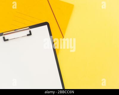 Scrivania da ufficio con piano orizzontale e vista dall'alto. Spazio di lavoro con blocco appunti, penna e notebook isolato su sfondo giallo stile minimo. Modello per Blo Foto Stock