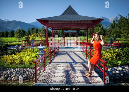 Ritratto di donna bella in abito arancione e hat vicino la pagoda nel giardino giapponese Foto Stock