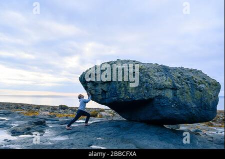 La donna pretende di sollevare Balance Rock, Skidegate, Haida Gwaii, precedentemente conosciuta come Queen Charlotte Islands, British Columbia, Canada Foto Stock