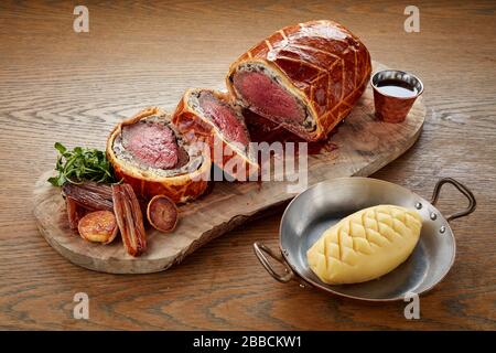 beef wellington intero affettato servito tavola di condivisione piatto legno carne di pasticceria rosa appena cotta Foto Stock