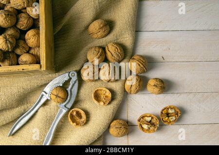 Noci in una scatola di legno, che si erge su un vecchio sacco rustico, anche sparsi su un tavolo bianco nelle vicinanze è un cracker di noce Foto Stock