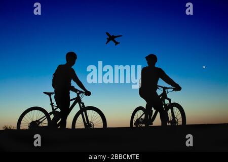 Due ciclisti sullo sfondo del cielo notturno e della luna, guardando l'aereo Foto Stock