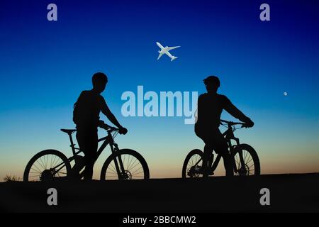 Due ciclisti sullo sfondo del cielo notturno e della luna, guardando l'aereo Foto Stock