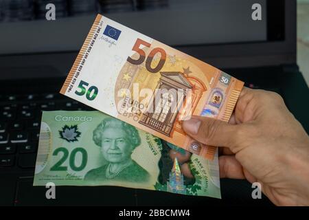 Una mano che detiene due banconote, una di venti dollari canadesi e l'altra di cinquanta euro Foto Stock