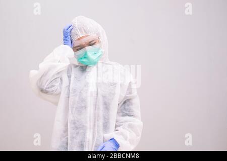 Stanca giovane infermiera che indossa tuta usa e getta con maschera e occhiali di sicurezza che pensano stanco e depressione sul problema Pandemic 2019 Coronavirus 2019- Foto Stock