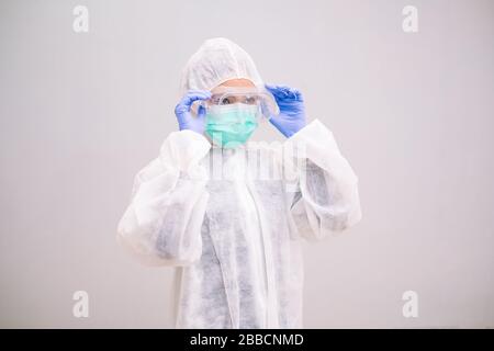 Infermiere giovane con tuta monouso indossando guanti sterili preparazione cura di Coronavirus 2019-nCoV pandemico 2019. Foto Stock