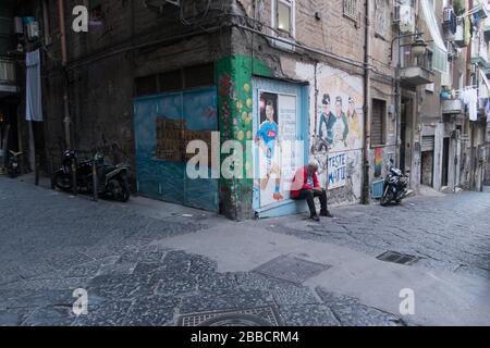 Un vecchio che controlla il suo telefono cellulare mentre si siede alla porta di un negozio con Napoli giocatori di calcio immagini sulle sue pareti Foto Stock
