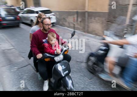 Una famiglia di tre persone che cavalcano illegalmente su uno scooter senza casco per le strade di Napoli Foto Stock