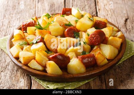 Ricetta di patate fritte con salsicce speziate e prezzemolo fresco primo piano in un piatto sul tavolo. Orizzontale Foto Stock