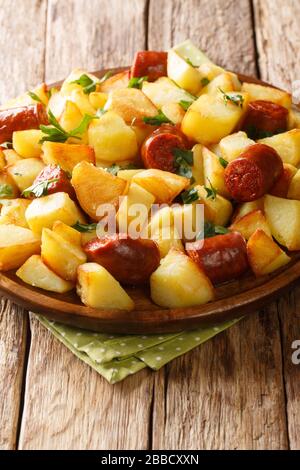 Fette di patate fritte con salsicce ed erbe primo piano in un piatto sul tavolo. Verticale Foto Stock