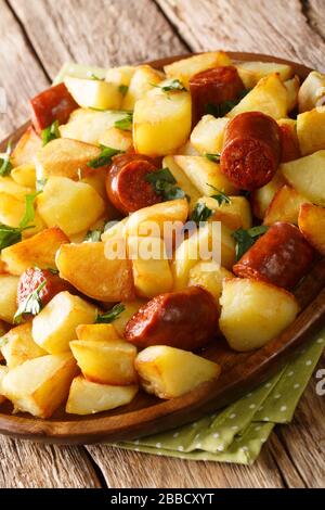 Patate fritte in stile rustico con salsicce e erbe primo piano in un piatto sul tavolo. Verticale Foto Stock