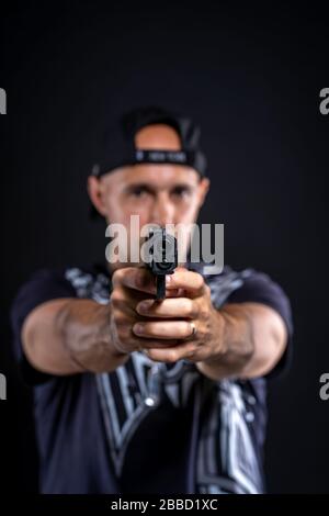 uomo che punta la pistola a oggetti, ritratto su sfondo nero Foto Stock