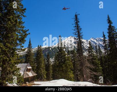 Chalet rimane nelle montagne innevate tra la foresta di conifere e elicottero di salvataggio nel cielo, Polonia, Tatra Foto Stock