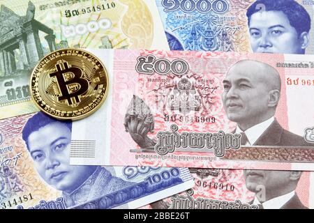 Primo piano su una moneta d'oro Bitcoin sopra una pila di banconote riel cambogiane. Foto Stock