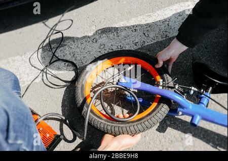 due persone senza facce pompano attraverso un filo nero la ruota di una bici da corsa arancione e blu sulla strada. lifestyle foto Foto Stock