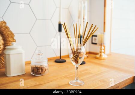 Tubi di carta oro per bevande in vetro in un'accogliente cucina in legno luminoso. Foto Stock