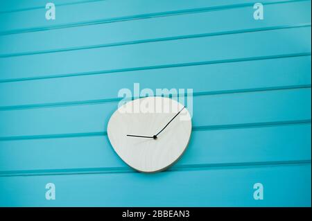 orologio minimalista in legno chiaro con mani nere senza quadrante su una parete blu brillante Foto Stock