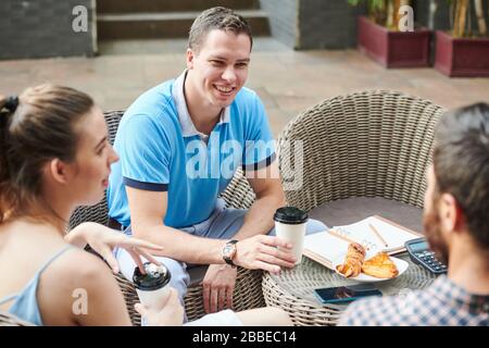 Felice bel giovane uomo d'affari caucasico bere caffè e ascoltare le idee dei colleghi di riunione in caffetteria Foto Stock