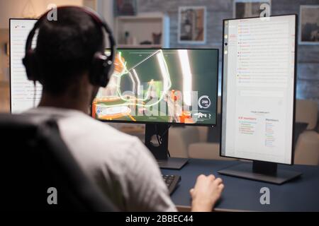 Vista posteriore dei giovani che giocano a videogame su computer con più monitor. Foto Stock