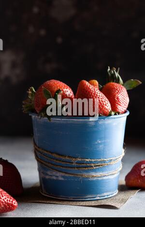 Bella fragola rossa in vaso blu. Fragole su sfondo nero scuro. Orizzontale. Minimalismo. Copia spazio per il testo. Foto Stock