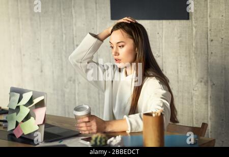Donna con caffè in mano guarda il laptop Foto Stock