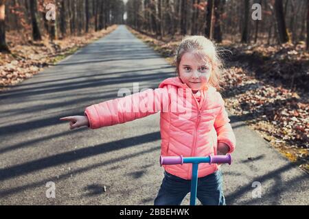 Bambina che gioca nel parco, guida uno scooter, divertirsi nella soleggiata giornata autunnale. Persone reali, situazioni autentiche Foto Stock