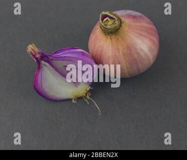 Una cipolla di colore rosa pelata a metà posta accanto a una cipolla di medie dimensioni non pelata prima di uno sfondo nero Foto Stock