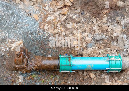 Un tubo di acqua comunale molto vecchio collegato ad un tubo nuovo. I tubi sono in sporco e ghiaia sul fondo di un foro. Il vecchio tubo perde da una ruggine Foto Stock